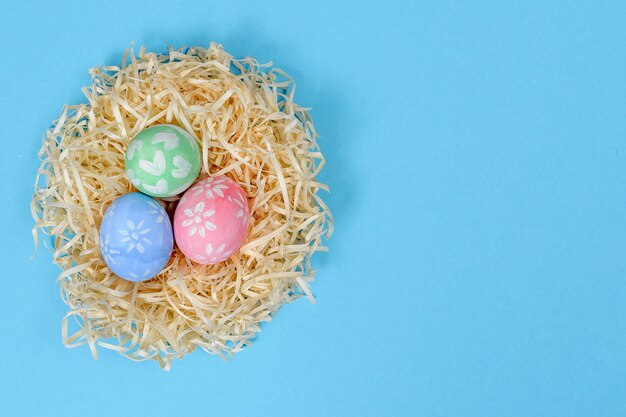 Oeufs de Pâques peints à la main colorés dans le nid isolé sur une surface bleue