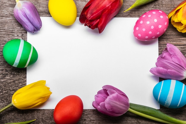 Oeufs de Pâques peints à la main avec des tulipes sur une carte de vœux vierge sur fond de bois copie espace pour texte