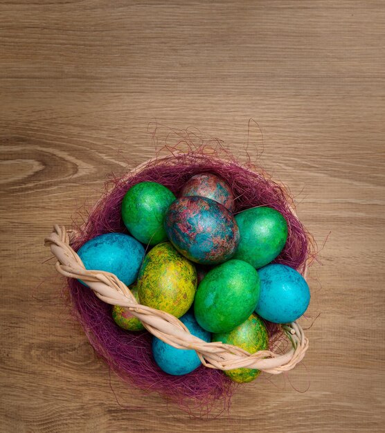 Photo oeufs de pâques peints multicolores dans un panier sur une vue de dessus de fond en bois