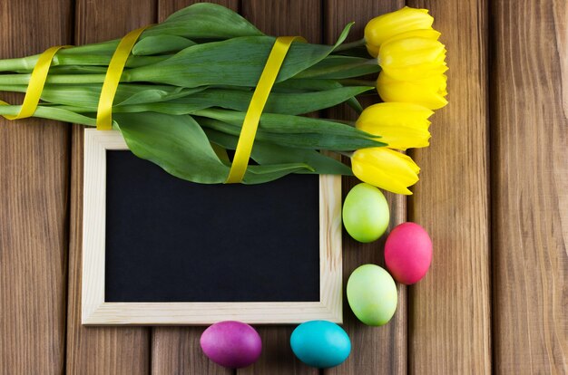 Oeufs de Pâques et une planche avec un cadre avec des tulipes jaunes