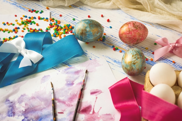 Les œufs de Pâques et le processus de coloration des œufs avant la fête. Rubans, oeufs, pinceaux, cadeaux sur la table en bois blanche