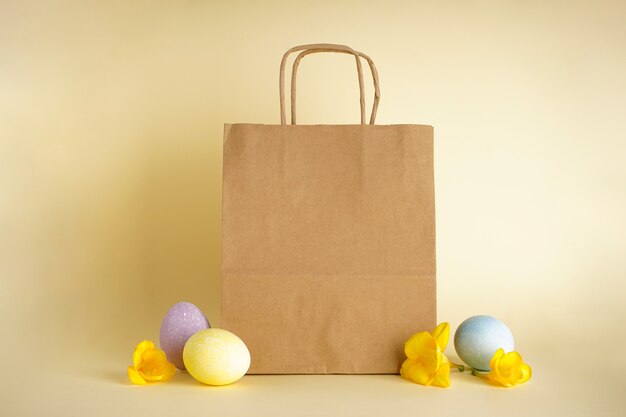 Oeufs de Pâques et sac en papier sur fond jaune.