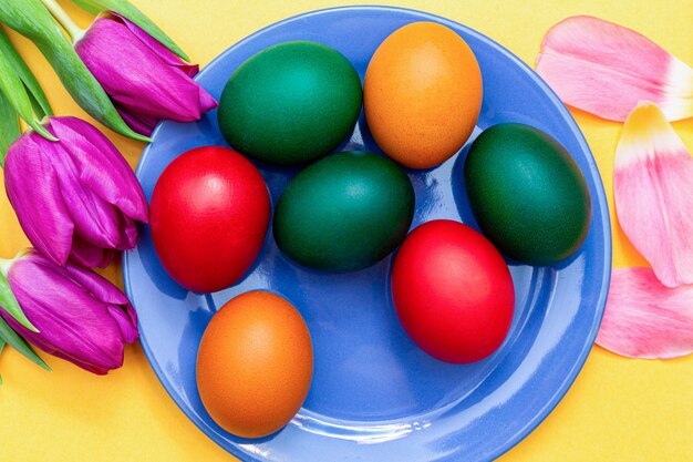 Oeufs de Pâques avec des tulipes sur un plat bleu sur un jaune.