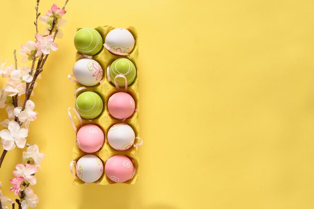 Oeufs pastel de Pâques dans une boîte en carton jaune et fleurs de printemps sur jaune.