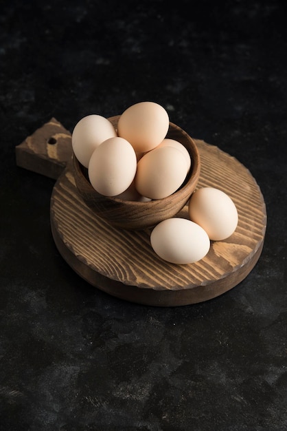 Oeufs sur planche de bois dans un bol en bois fond sombre