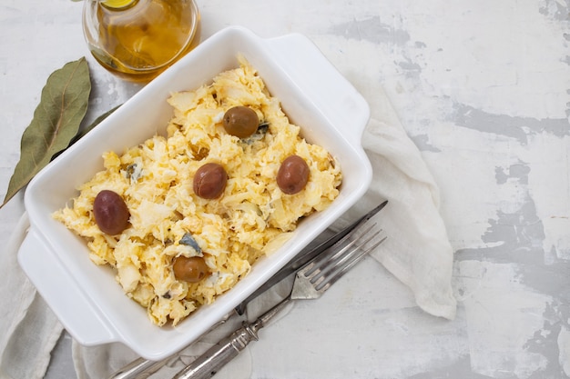 Œufs de plat typiquement portugais avec morue et olives dans un plat blanc Bacalhau a lisbonense