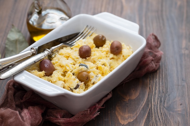 Œufs de plat typiquement portugais avec morue et olives dans un plat blanc Bacalhau a lisbonense