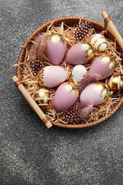 Oeufs et plumes dorés et roses dans une assiette en osier