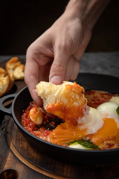 oeufs pochés, avec tomates et sauce dans une casserole sur une planche de bois