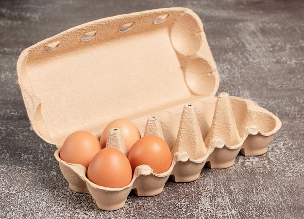 Oeufs de poule bio frais dans un carton ouvert ou un récipient à oeufs sur fond marron