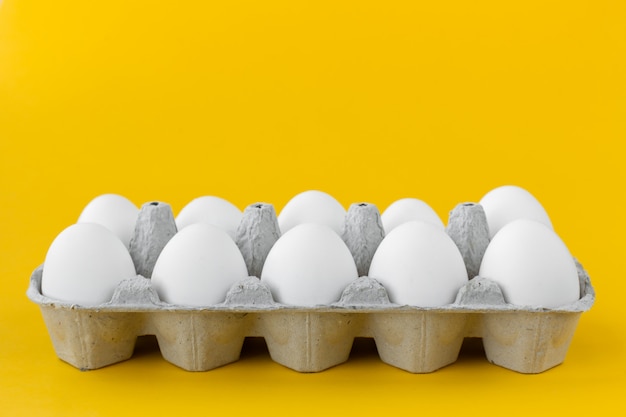 Oeufs de poule blanche dans un carton ouvert sur fond jaune