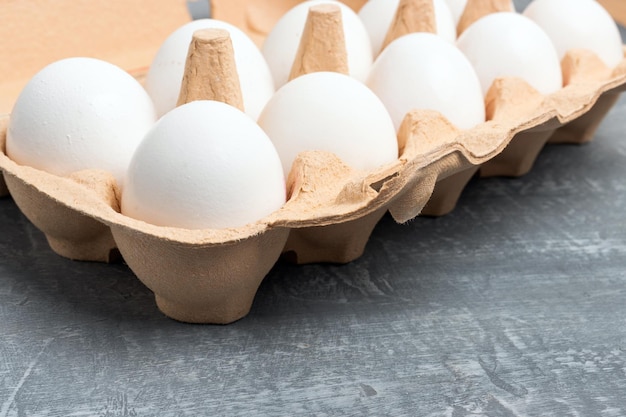 Photo oeufs de poule blancs dans une boîte en carton sur fond texturé gris