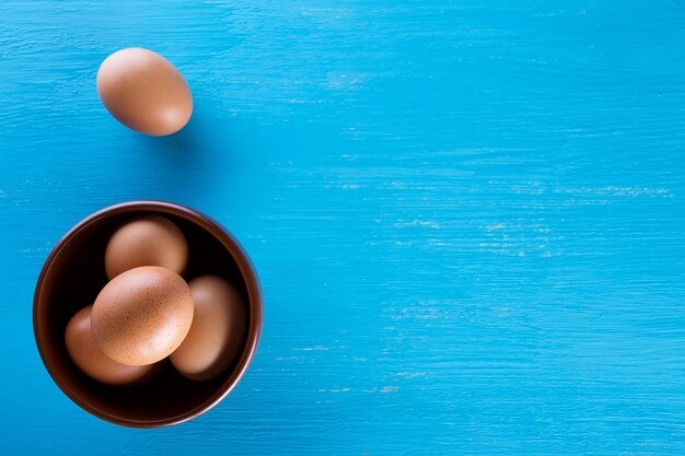 Oeufs de poule brune dans une soucoupe sur une table en bois bleue