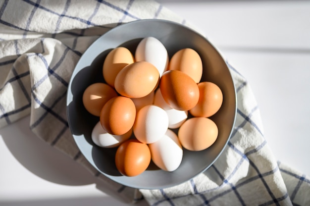 Oeufs de poule de couleur blanche et brune dans une assiette grise sur un torchon vérifié