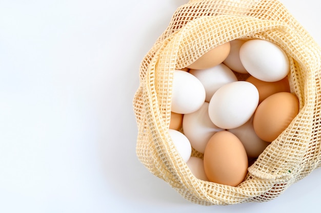 Oeufs de poule de couleur blanche et marron dans un sac en filet réutilisable beige