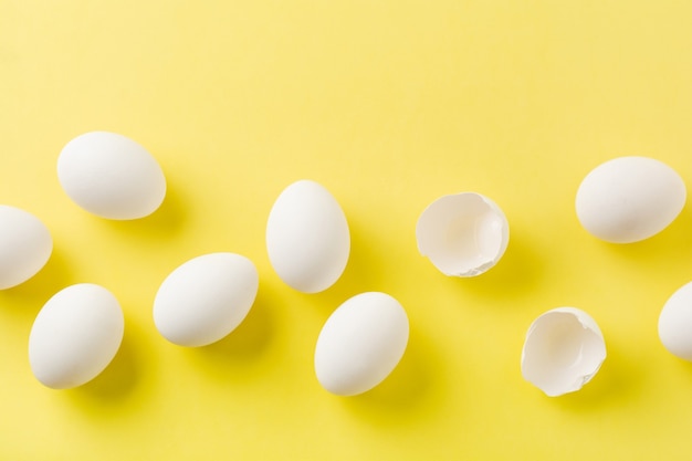 Oeufs de poule crus blancs couchés dans la rangée horizontale avec oeuf cassé sur une surface jaune. Vue de dessus.