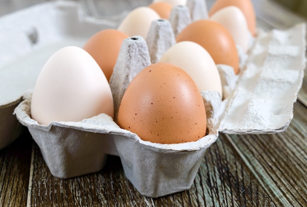 Oeufs de poule crus frais dans une boîte à œufs en carton sur fond de bois. Vue rapprochée sur les œufs bruns et blancs.