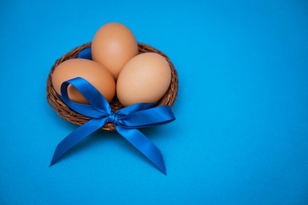 Oeufs de poule dans un bol de paille avec un arc bleu sur fond bleu,