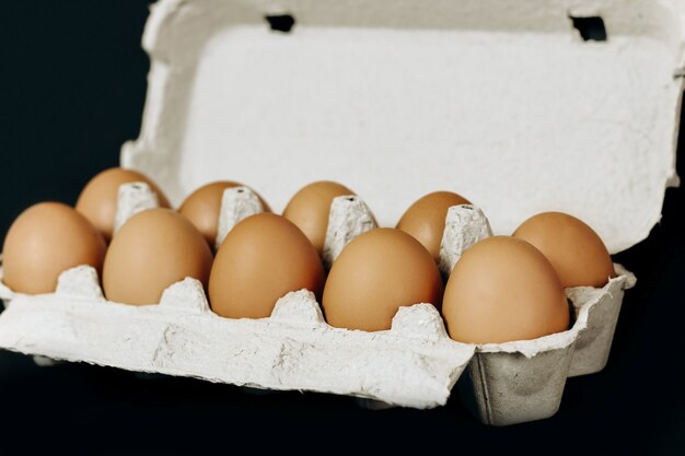 Oeufs de poule dans une caisse grise en papier sur fond noir