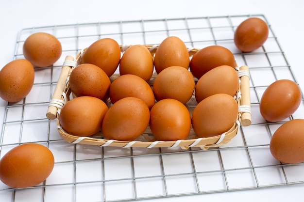 Oeufs de poule dans un panier en bambou sur blanc.