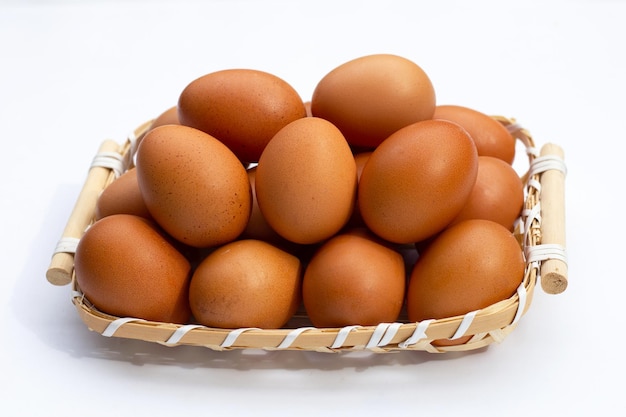 Oeufs de poule dans un panier en bambou sur blanc.