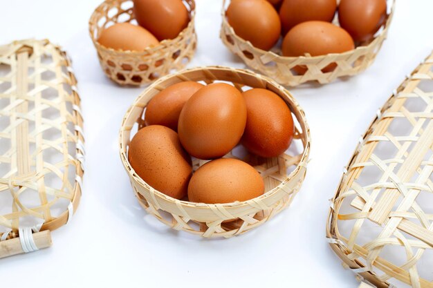 Oeufs de poule dans un panier en bambou sur blanc.