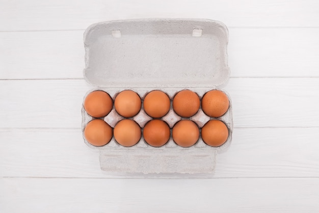 Oeufs de poule dans un plateau en carton isolé sur une surface en bois blanche.