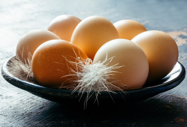 Oeufs de poule frais et plumes dans une assiette sur la table dans un matin rustique