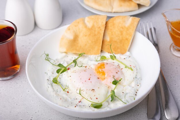 œufs turcs chilbir avec yogourt beurre parfumé pousses de pois pain plat et thé petit déjeuner turc traditionnel avec œufs pochés avec jaune liquide focus sélectif de près