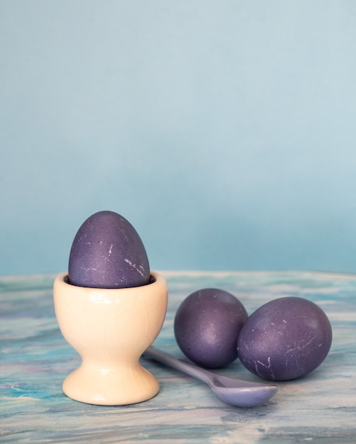 Oeufs violets peints et cuillère en porcelaine de la couleur des oeufs sur fond bleu