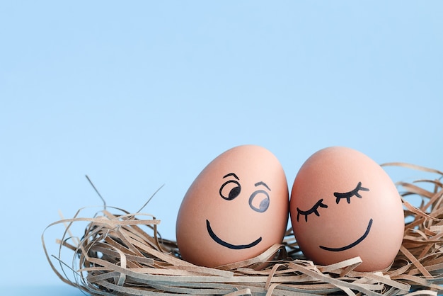 Oeufs avec des visages souriants sur eux se trouvent dans le nid avec un fond bleu clair