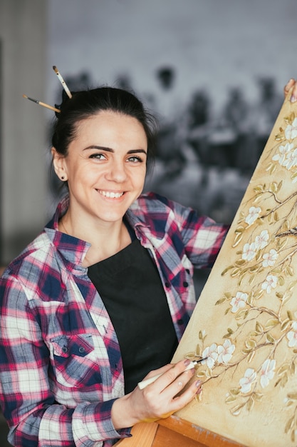 Oeuvre en cours. Inspirations d'atelier. Artiste femme souriante avec outil. Toile sur chevalet. Texture de motif de fleurs et d'oiseaux.