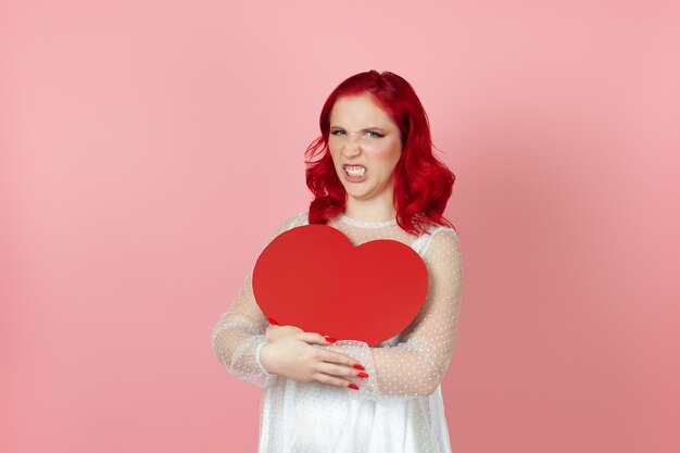 Offensé femme en robe blanche et aux cheveux rouges tenant un grand coeur de papier rouge