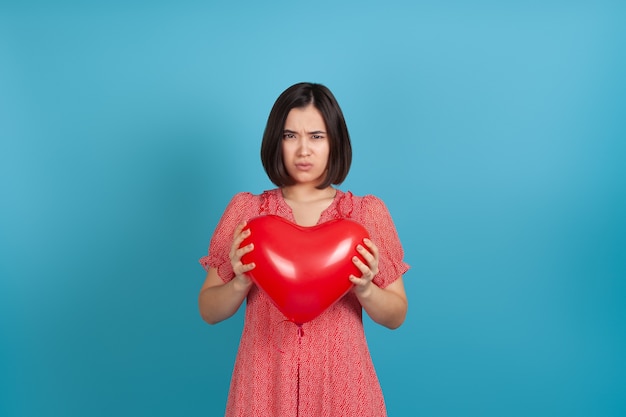 offensée par un mauvais cadeau, une jeune femme asiatique tient un ballon rouge en forme de cœur dans ses mains