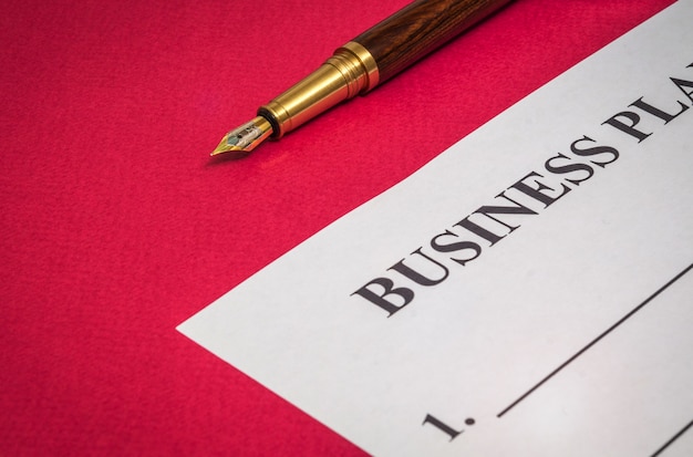 Office nature morte sur table rouge avec un stylo doré et un plan d'affaires se prépare pour les notes