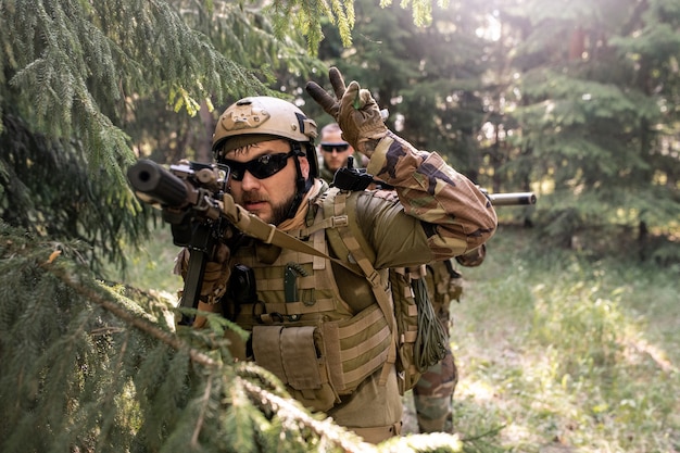 Officier barbu en casque et lunettes de soleil compte à rebours avant l'attaque lors d'une opération militaire en forêt