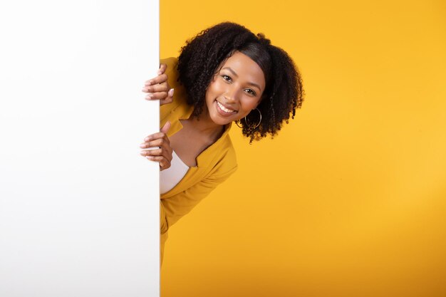 Photo offre intéressante happy black lady lorgnant sur le côté du panneau publicitaire blanc pour votre texte ou