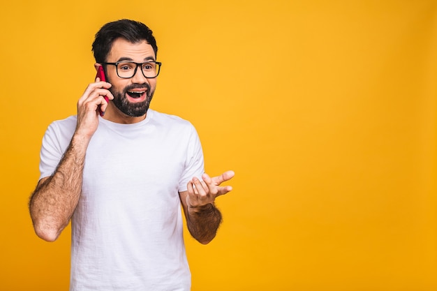 Oh, bonne nouvelle! Souriant jeune homme barbu occasionnel, parler au téléphone isolé sur fond jaune.