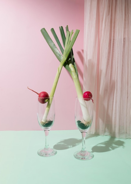 Photo l'oignon et l'ail de printemps dans des verres de champagne séparés sur un fond rose pastel et de menthe