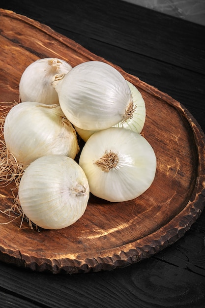 Oignons blancs sur une planche de bois sur fond noir. Alimentation biologique