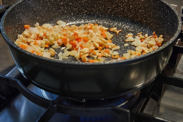 Les oignons et les carottes sont frits dans une poêle sur une cuisinière à gaz