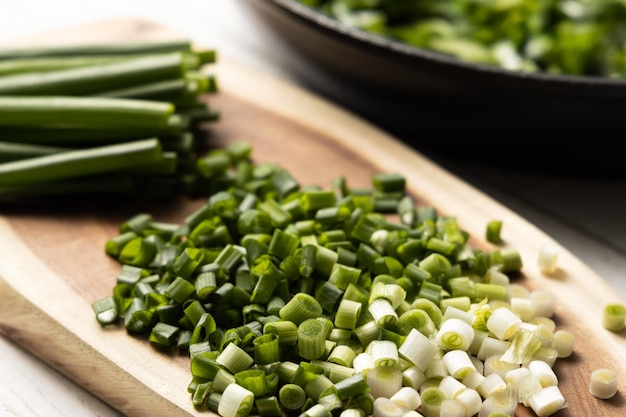 Oignons verts coupés sur une planche de bois En arrière-plan une casserole noire