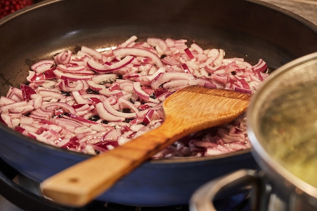 Les oignons violets sont frits dans une poêle sur une cuisinière à gaz