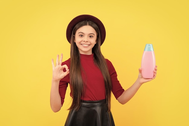 Ok happy girl in hat hold shampooing présentant un produit cosmétique pour adolescent