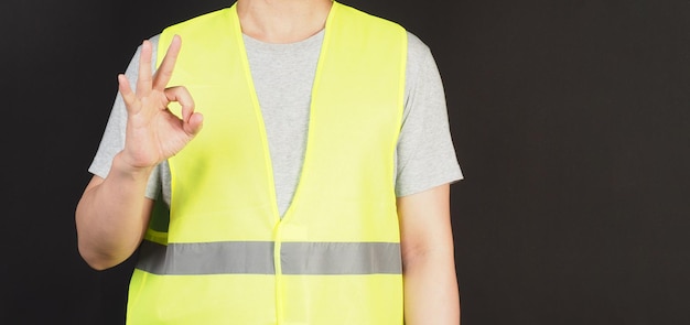 OK Sign de la main et l'homme porte un gilet de sécurité sur fond noir