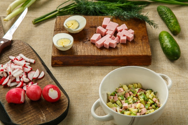 Okroshka dans une soupière sur la table sur une nappe à côté de légumes sur des planches. photo horizontale