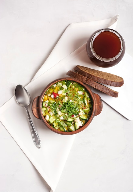 Un okroshka russe avec des légumes frais et de la viande dans une tasse d'argile se dresse sur un gris