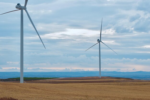 Éoliennes sur un champ coupé avec des nuages spectaculaires Générateurs d'énergie alternative contre le ciel bleu avec des nuages dans la région de Teruel Aragon Espagne Site de production d'électricité