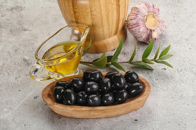 Des olives noires dans le bol avec de l'huile et des branches