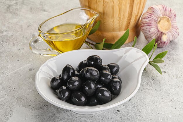 Des olives noires dans le bol avec de l'huile et des branches